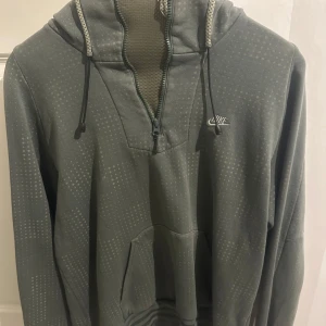 Grå hoodie från Nike - Säljer en grå hoodie från Nike med dragkedja och justerbar huva. Tröjan har ett diskret mönster och en praktisk magficka. Perfekt för en avslappnad stil.