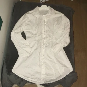 Vit långärmad skjorta - Klassisk vit långärmad skjorta med knappar framtill. Perfekt för en stilren look. Skjortan har en enkel design med krage och manschetter. Har dock ingen aning om vart den är ifrån då lappen är borttagen 