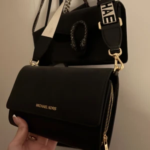 Svart axelväska från Michael Kors - Snygg svart axelväska från Michael Kors med justerbar axelrem och gulddetaljer. Väskan har en stilren design med logotyp framtill. nypris: runt 1700kr 💗, använt 1 gång!