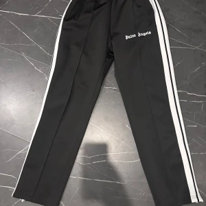  Palm Angels byxor  - Snygga svarta byxor från Palm Angels med vita sidoränder och logga på framsidan. Tillverkade i polyester för en bekväm passform. Perfekta för en avslappnad stil.
