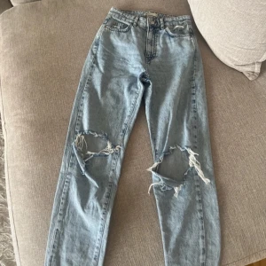 Blåa jeans - Snygga ljusblå jeans med slitningar på knäna från gina tricot. De har en klassisk femficksdesign och knappgylf. Perfekta för en avslappnad stil. Säljer då de är för stora för mig