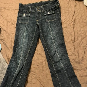 Mörkblå jeans med fickdetaljer - Snygga mörkblå jeans med unika fickdetaljer och dubbla knappar i midjan. Byxorna har en klassisk bootcut-stil och är perfekta för en avslappnad look. De har en lågmidjad passform och är tillverkade i ett slitstarkt denimtyg.💕
