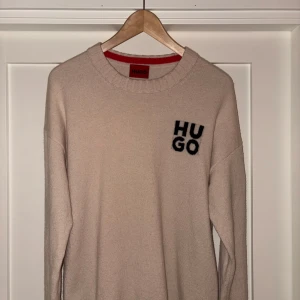 Hugo boss stickad tröja  - Säljer en stilren beige tröja från Hugo boss med svart logotyp på bröstet. Tröjan har en rund halsringning och långa ärmar. Perfekt för en avslappnad och trendig look.                                            Storlek L.                                                                                       Nypris (1800kr)                        