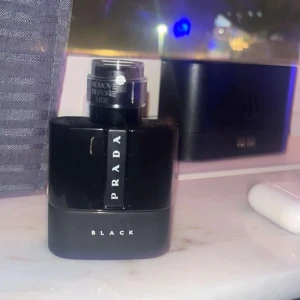 Prada Black parfym - Elegant och stilren parfymflaska från Prada i svart med texten 'BLACK'. Flaskan har en modern design med en praktisk sprayfunktion. Perfekt för den som söker en sofistikerad doftupplevelse. Helt ny endast testad