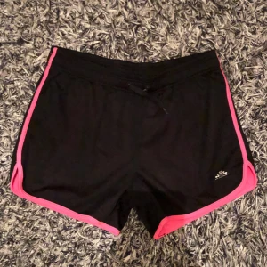 Träningsshorts med rosa detaljer - Svarta träningsshorts med rosa kantdetaljer. Har en elastisk midja med snörning för justerbarhet. I barnstorlek 158/164! 