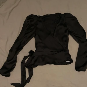 Svart omlottblus från Gina Tricot - Svart omlottblus från Gina Tricot i silkestyg, puffärmar med liten axelvadd.                                              Kolla gärna min profil, säljer mycket nu, allt i fint skick och till bra pris