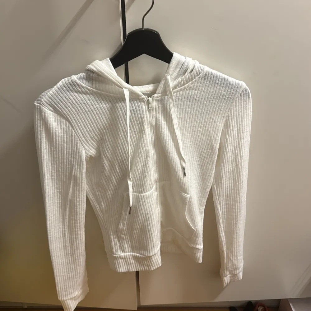 Säljer en stilren vit ribbad hoodie från Dazy. Den har en dragkedja framtill och en praktisk huva med snörning. Perfekt för en avslappnad look. Använd 2 gånger!!. Neuletakit & Villapaidat.