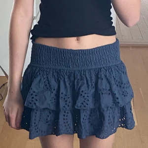 Kjol från Meet me there - Nypris: 500kr. Söt mörkblå lågmidjad kortkjol med volanger och broderade detaljer från Meet me there. Väldigt bekväm, luftig design och elastiska midja. Använd 1 gång, nyskick och inga defekter. 
