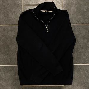 Svart tröja med dragkedja från Jack & Jones - Snygg svart tröja från Jack & Jones med dragkedja vid halsen. Perfekt för kyligare dagar med sin ribbade design och långa ärmar. En stilren och mångsidig tröja för alla tillfällen.