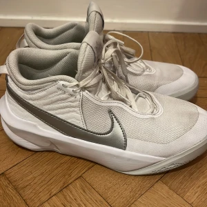 Vita och silverfärgade Nike sneakers - Snygga vita Nike basket  sneakers med silverdetaljer och snörning. Perfekta för en sportig look med bekväm passform och slitstark sula.