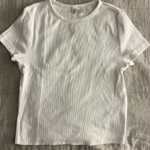 Vit ribbad t-shirt från Hm - Säljer en stilren vit ribbad t-shirt från Hm. Den har en klassisk rund hals och korta ärmar, perfekt för en avslappnad look. Passar till det mesta i garderoben!