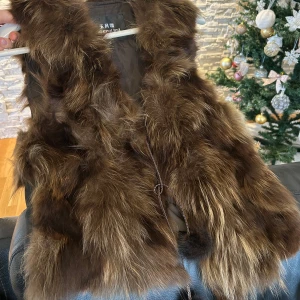 Brun pälsväst från YuFengLing - Säljer en snygg brun pälsväst från YuFengLing. Västen har en fluffig och lyxig känsla med en knytning framtill. Perfekt för att hålla sig varm och stilren under kyliga dagar. Funkar som en S/M