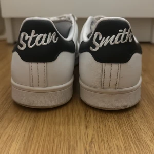 Vita Adidas Stan Smith sneakers - Klassiska vita Adidas Stan Smith sneakers med svart hälflik och snörning. Perfekta för en stilren look. Ord pris 779 kr.