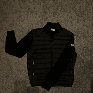 Moncler cardigan - Snygg svart pufferjacka från Moncler med dragkedja och ribbade detaljer. Jackan har långa ärmar och Moncler-logga på ärmen. Perfekt för kyligare dagar. Nypris 10,900 
