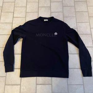 Äkta mörk blå tröja från Moncler - Säljer en stilren svart tröja från Moncler. Den har en klassisk design med rund hals och långa ärmar. Perfekt för både vardag och lite finare tillfällen. Moncler-loggan syns diskret på bröstet. Passar bra till höst och vinter. Hör er av om ni vill ha fler bilder. Priset är inte hugget i sten💯
