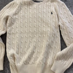 Vit stickad tröja från Polo Ralph Lauren - Säljer en klassisk vit stickad tröja från Polo Ralph Lauren. Den har ett snyggt kabelstickat mönster och är i mycket bra skick. Perfekt för både höst och vinter, med långa ärmar och ribbade muddar. En tidlös favorit i garderoben! 🤍