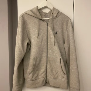 Grå hoodie från Ralph Lauren - Säljer en stilren och bekväm grå hoodie från Ralph Lauren. Den har en dragkedja framtill och en klassisk logga på bröstet. Perfekt för både vardag och chill. Passar bra till höst och vår. Den är varsamt använd i ungeäfr ett år. 💯💯den är storlek S men