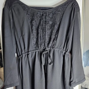 Svart blus från Vero Moda - Snygg svart blus från Vero Moda i storlek L. Den har trekvartsärmar och en vacker spetsdetalj fram och på ryggen. Blusen har en knytning i midjan för en smickrande passform. Perfekt för både vardag och fest! Inga defekter. 