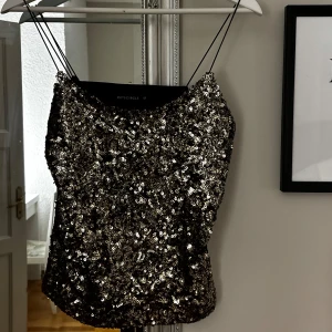 Svart paljettlinne från Butik - Snyggt svart linne med glittrande paljetter över hela framsidan. Linnet har tunna axelband och en enkel design som passar perfekt för festliga tillfällen. Baksidan är i ett slätt svart tyg vilket ger en fin kontrast till de glittriga paljetterna framtill.