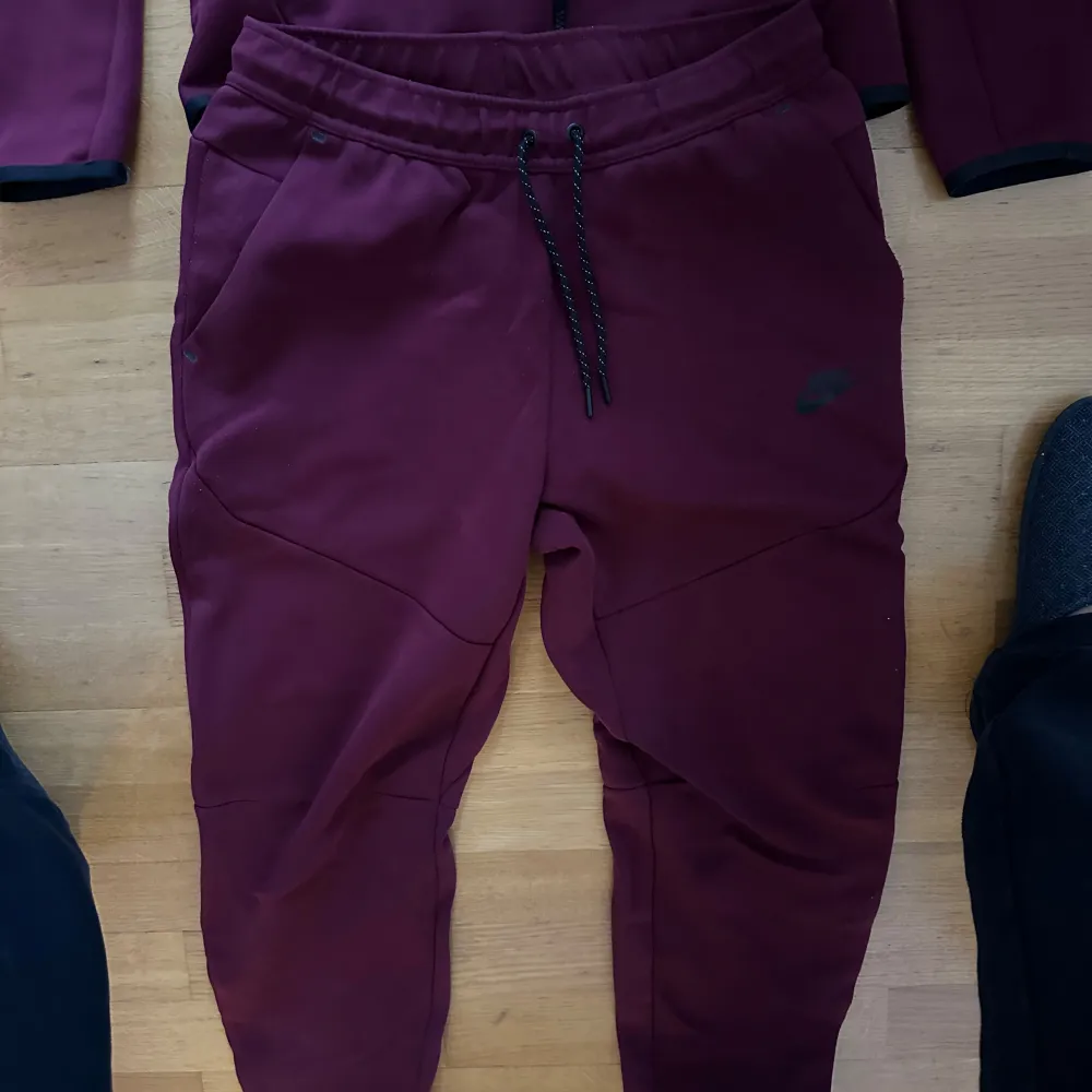 Säljer ett set med vinröd hoodie och matchande byxor från Nike. Hoodien har dragkedja och en snygg detalj i form av ett grått mönster över bröstet. Byxorna har en bekväm passform med dragsko i midjan. Perfekt för en avslappnad stil eller träning. Storlek S i koftan och M i byxorna.. Tröjor & Koftor.