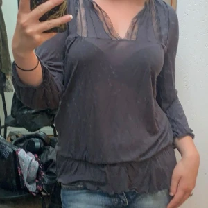 Grå blus med spetsdetaljer - Säljer en snygg grå blus med spetsdetaljer vid halsen. Blusen har trekvartsärmar och en lös passform, perfekt för både vardag och fest. Den är i bra skick och superbekväm att ha på sig. Passar perfekt till jeans eller kjol!