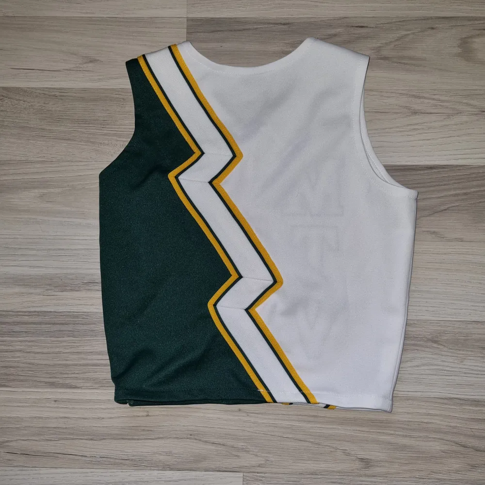 Säljer en grön och vit ärmlös cheerleadingtopp med bokstäverna 'MTV' i gult och grönt. Toppen har en cool zigzag-design och en liten megafonbrodering. Perfekt för sportiga tillfällen eller som en retro modeaccessoar. Den har en dragkedja på sidan för enkel på- och avtagning. Sömmen på M har släppt men går lätt att sy.. Toppar.