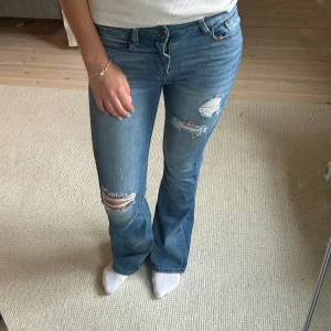 Jeans med slitningar - Säljer ett par snygga blå bootcut jeans med coola slitningar. Midjemått: 36cm, Innerbenslängd: 83cm