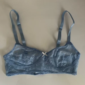 Ljusblå spets-bh med rosett - Säljer en elegant ljusblå spets-bh med en söt liten rosett framtill. Den har justerbara axelband för perfekt passform. Perfekt för att känna sig både bekväm och stilren. Passar till både vardag och speciella tillfällen.