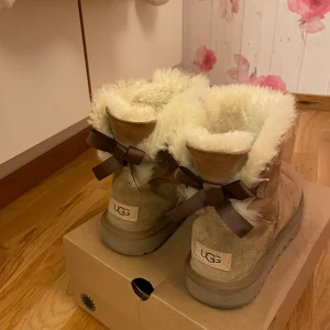 Uggs 🎀 Mini Bailey Bow II - Super sköna och mysiga Uggs i färgen ”Chestnut” till både höst och vinter🍂❄️ Bortsett från fläcken av snö är skorna i väldigt bra skick, men dock säljer jag till någon som kanske är mer utefter funktionalitet. 