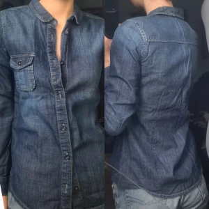 Jeansskjorta mörkblå 36 - Nyskick men gammal. 100% bomull. Lite korta ärmar på mig. Kameran fick inte till färgen så fick försöka redigera fram den, men det är rätt saturated, klassisk, mörkblå jeansfärg. Vidd 40-47, längd 66, ärmlängd 61.