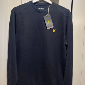 Mörkblå tröja från Lyle & Scott - Säljer en snygg mörkblå tröja från Lyle & Scott. Den har en enkel design med deras ikoniska gula logga på bröstet. Tröjan är långärmad och perfekt för både vardag och lite finare tillfällen. Den är aldrig använd och har även lappen kvar nypris 899kr