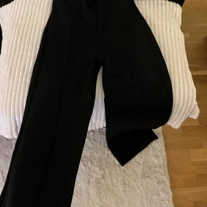 Svarta kostymbyxor - Säljer ett par eleganta svarta kostymbyxor. De har en klassisk design med en rak passform och hög midja. Perfekta för både formella tillfällen och kontoret. Byxorna är i nyskick och har en stilren look.