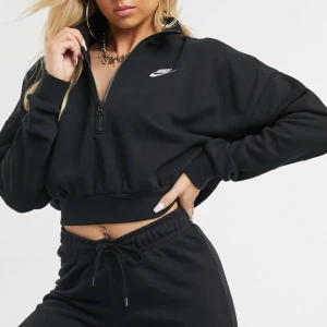 Svart croppad hoodie från Nike - Svart croppad tröja från Nike. Den har en halv dragkedja framtill och det klassiska Nike-loggan i vitt på bröstet. Storlek S. Fint skick.