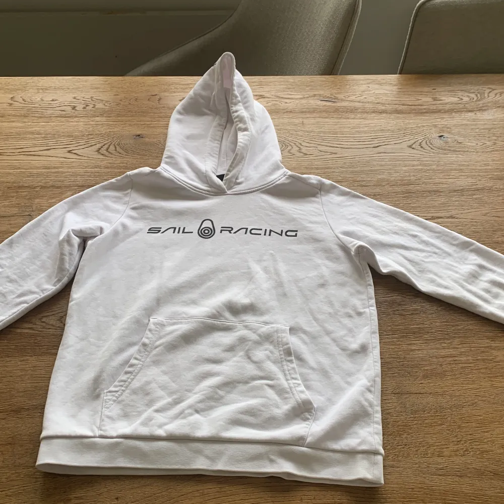 Säljer en snygg vit hoodie från Sail Racing. Den har en klassisk design med en stor ficka framtill och en bekväm huva. Perfekt för en avslappnad stil eller kyliga dagar. Den är i bra skick och redo för nya äventyr!. Hoodies.