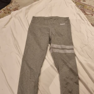 Grå leggings från Stronger - Säljer ett par grå/gröna leggings från Stronger i storlek small. De är gjorda av 87% polyester och 13% elastan, vilket gör dem superstretchiga och bekväma. Perfekta för träning eller en chill dag hemma. De har en snygg detalj med prickar på ena benet