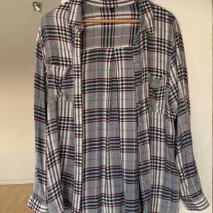Rutig skjorta i grått, vitt och rött - Säljer en stilren rutig skjorta i grått, vitt och rött. Skjortan har långa ärmar och knappar framtill. Perfekt för en avslappnad look. Tyget är ganska tunt. Pris går att diskutera vid snabb affär. Tveka inte att höra av dig vid frågor och funderingar.