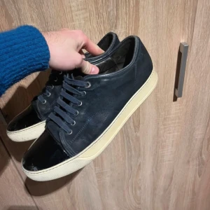 Lanvins - Snygga mörkblå sneakers från Lanvin med vita sulor och snörning. Skorna har en stilren design med en svart blank tådel och är perfekta för en casual look. Väldigt fint skick och är i storlek 43 och box ingår 