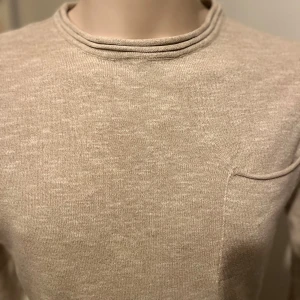Beige långärmad tröja från WINWIN - Säljer en stilren beige långärmad tröja från WINWIN. Tröjan har en enkel bröstficka och är tillverkad i ett mjukt material som ger en skön känsla. Perfekt för en avslappnad look.