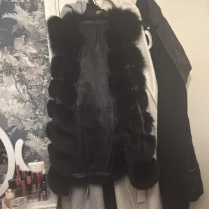 Svart pälsväst i äkta läder och äkta päls - Snygg svart pälsväst i äkta läder och päls, med dragkedja. Perfekt för att ge en lyxig touch till din outfit. Västen har en elegant design med mjuk päls som ger extra värme och stil.