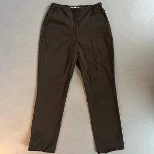 Grönbruna kostymbyxor - Supersköna kostymbyxor i en snygg grönbrun färg! Medelhög midja och perfekt längd, är 158. Fickor i sidan, men hopsydda på baksidan. 