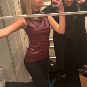 Vinröd ärmlös topp - Snygg vinröd ärmlös topp i ett glansigt/ fejk läder material. Perfekt för en kväll ute eller en speciell tillställning. Toppen har en figurnära passform som framhäver silhuetten.