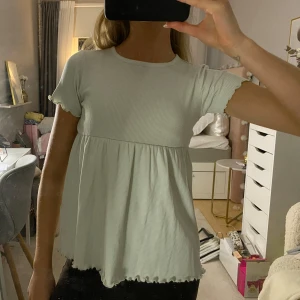 Mintgrön ribbad topp - Säljer en söt ljusgrön ribbad topp med volangdetaljer. 