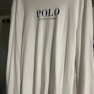 Vit långärmad tröja från Polo Ralph Lauren - Säljer en stilren vit långärmad tröja från Polo Ralph Lauren med deras klassiska logotyp tryckt i blått på framsidan. Perfekt för en avslappnad och snygg look. Använd 3 gånger. 