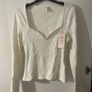 Vit ribbad topp från Nelly - Säljer en stilren vit ribbad topp från Nelly med långärmad design och en elegant v-ringning. Den  är aldrig använd och säljs med prislapp. 🤍✨