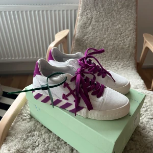 Vita sneakers från Off-White - Snygga vita sneakers från Off-White med lila detaljer och snörning. Skorna har ett unikt mönster med diagonala ränder på sulan och Off-White-logotypen på sidan. Använda en gång. Box och dustbag finns med. 