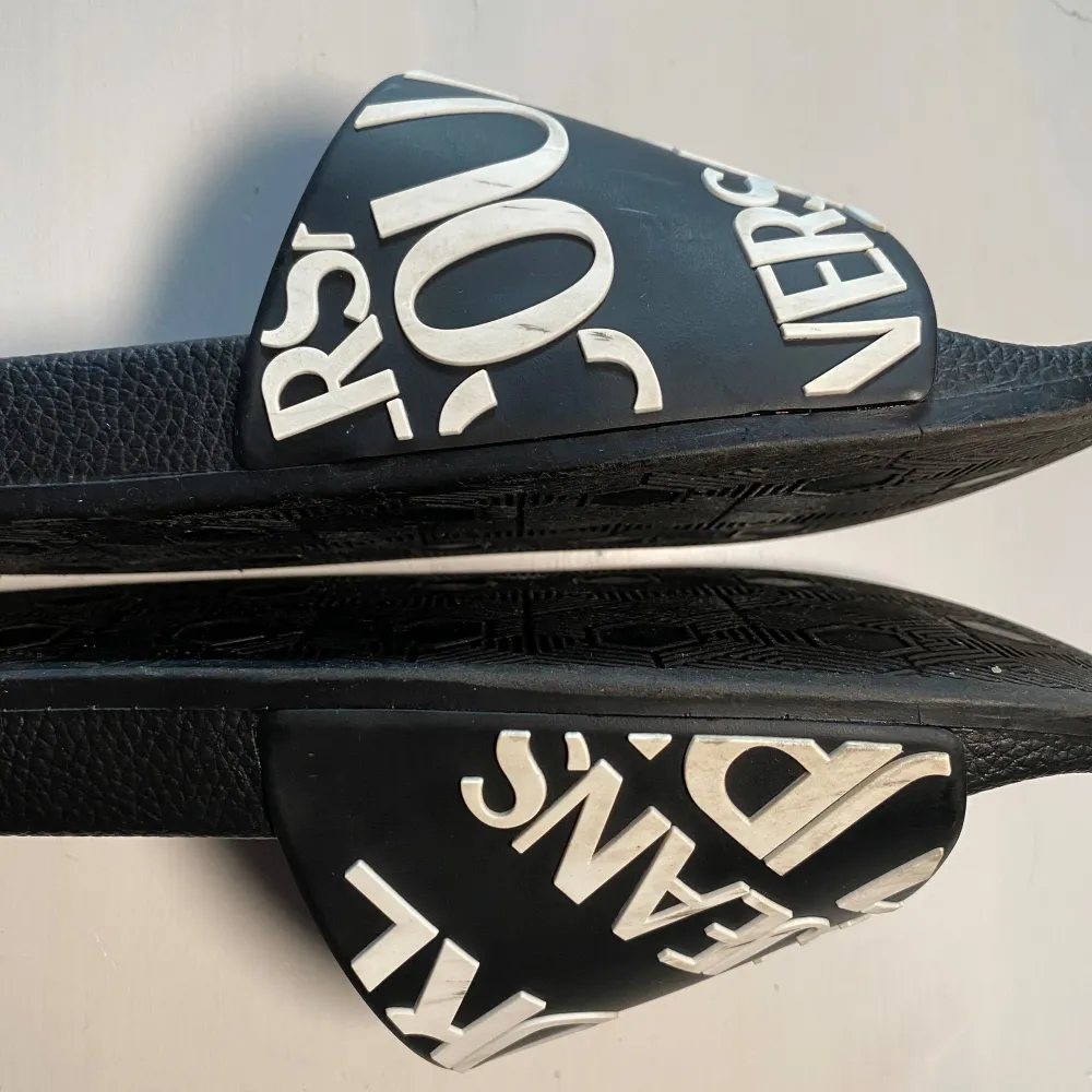 Snygga svarta sandaler med vit text på ovandelen. Sandalerna har en bekväm sula med mönstrad undersida för bra grepp. Perfekta för en avslappnad stil. Jag har storlek 43 och dom sitter lita tajt på mig. Jag gissar att dom är storlek 41-42. . Kengät.