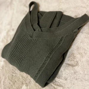 Stickad tröja från Hollister - Säljer en snygg grön stickad tröja från Hollister med offshoulder-design. Tröjan har långa ärmar och ribbade kanter, vilket ger en stilren look. Perfekt för kyligare dagar!