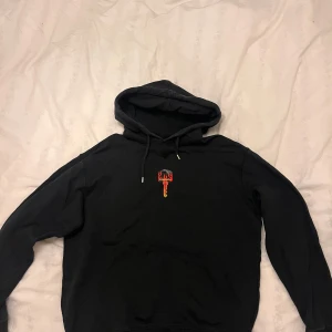 Svart hoodie från DSQUARED2 - Säljer en svart hoodie från DSQUARED2 med en cool nyckeltryck i rött och gult på bröstet. Hoodien har en klassisk design med dragsko i huvan och långa ärmar. Perfekt för en SUPERSTAR stil!