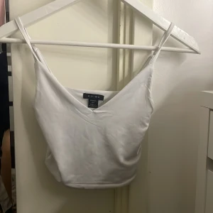 Vit linnetopp från Amisu/new Yorker  - Säljer en stilren vit linnetopp från Bik Bok. Toppen har smala axelband och en v-ringad design som ger en enkel och fräsch look. Perfekt för varma dagar eller som ett basplagg i garderoben.