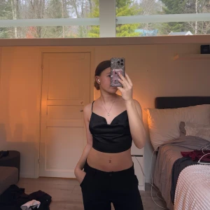 Svart satinlinne med öppen rygg - Snyggt svart satinlinne med smala axelband och öppen rygg. Linnet har en elegant snörning i ryggen som ger en unik look. Perfekt för en stilren och festlig outfit.